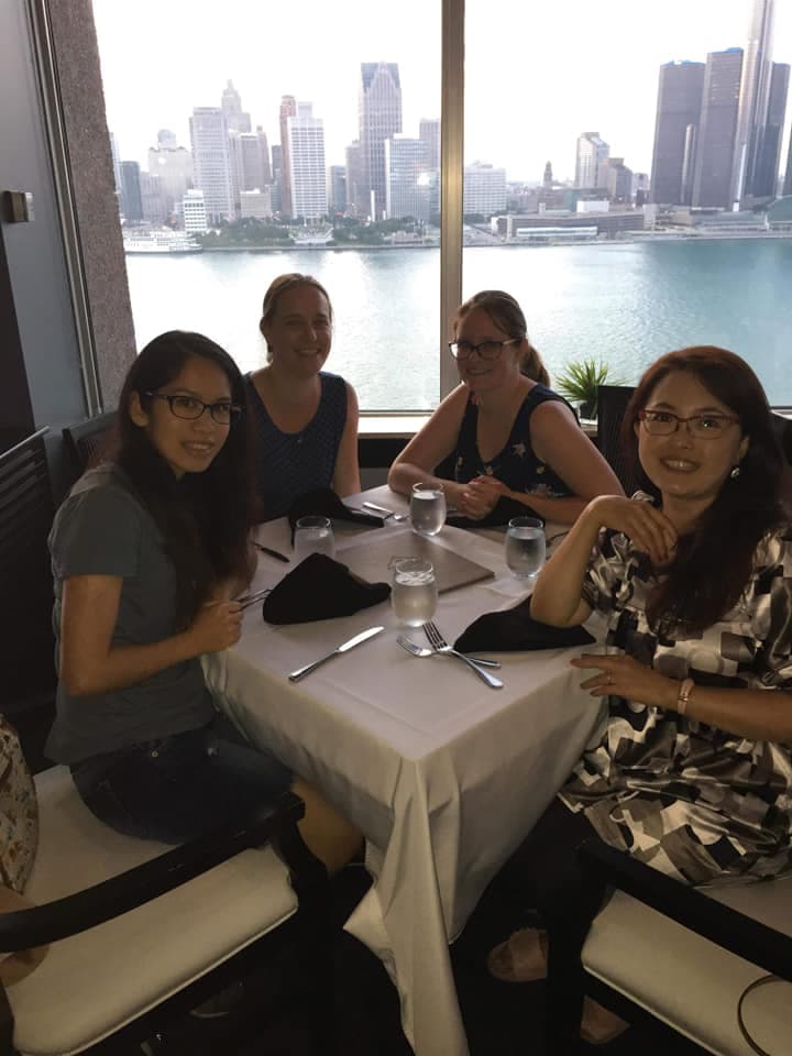 Four women at a white-tablecloth restaurant with a city skyline behind them